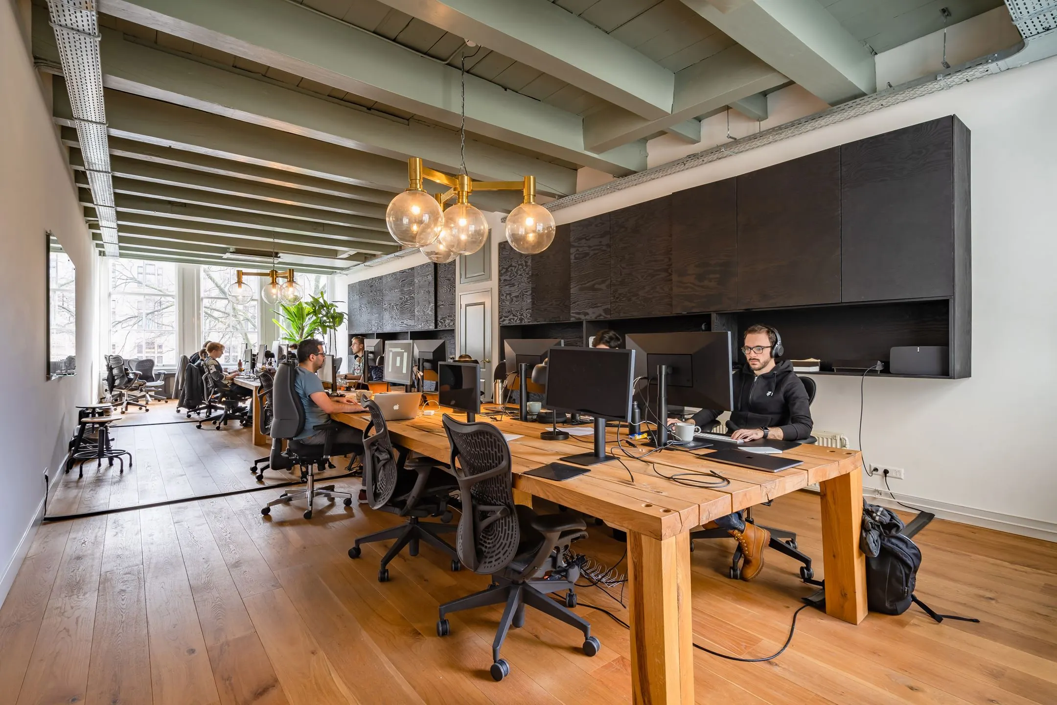 Open kantoorruimte aan de Singel 258 met houten vloer, lange werktafel, meerdere werkplekken en mensen aan het werk achter computers.