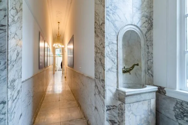 Marmeren gang in Singel 258 met klassieke wandfontein en kroonluchterverlichting.