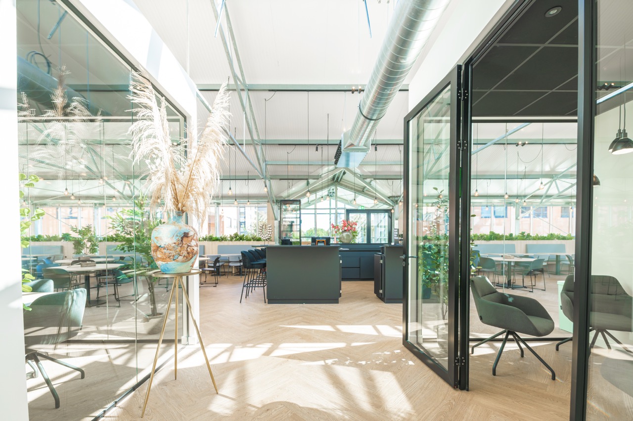 Licht en modern interieur van Sociaal Hart 15 met glazen wanden, planten en een centraal ontmoetingspunt.