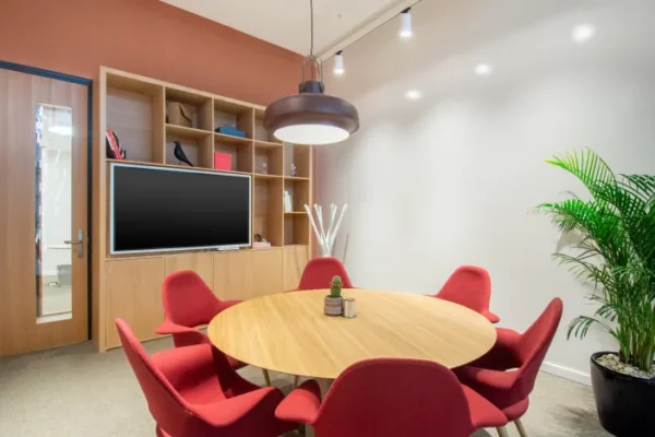 Kleine vergaderruimte in Spaces Riyadh Park met ronde houten tafel, rode stoelen, flatscreen-tv en moderne inrichting.