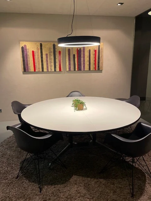 Ronde tafel met vijf stoelen in een moderne spreekkamer, verlicht door een hanglamp en met kunst aan de muur.