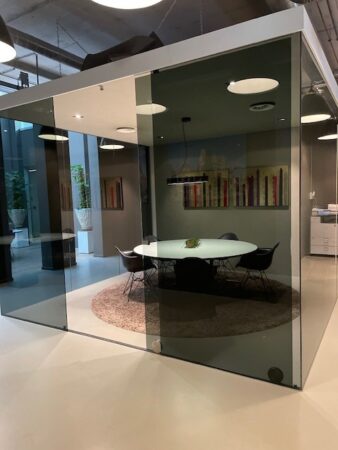 Glazen spreekkamer met ronde tafel en stoelen in een modern kantoorgebouw.