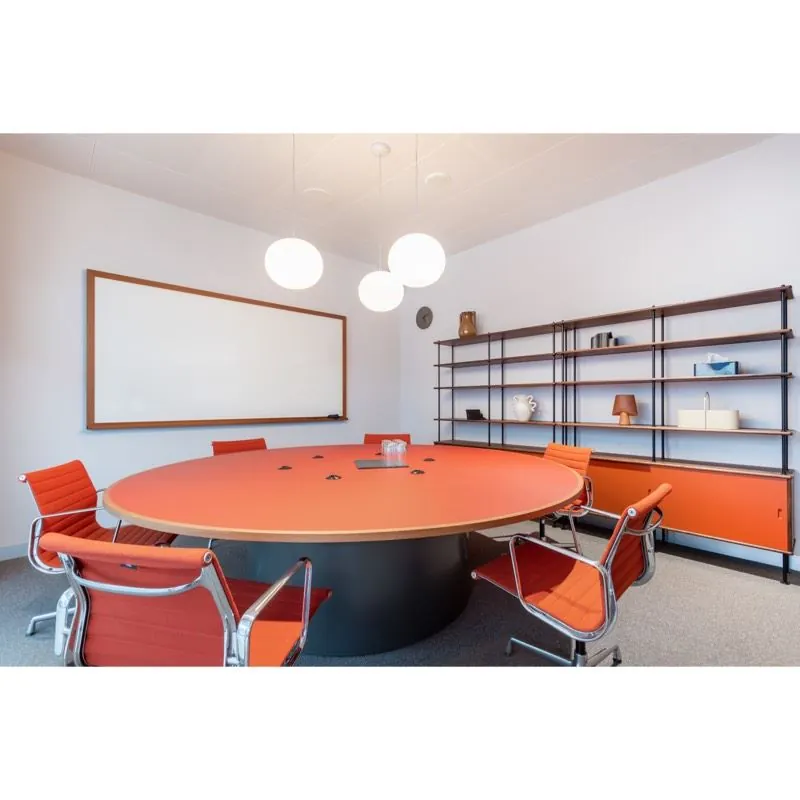Vergaderruimte met een grote ronde oranje tafel, bijpassende stoelen en een wandrek, gelegen aan Stadsplateau 27-29.
