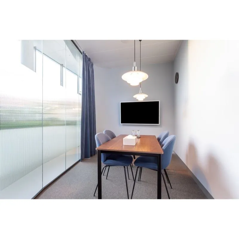 Vergaderruimte met een houten tafel, vier blauwe stoelen, hanglampen en een flatscreen aan de muur in Stadsplateau 27-29.