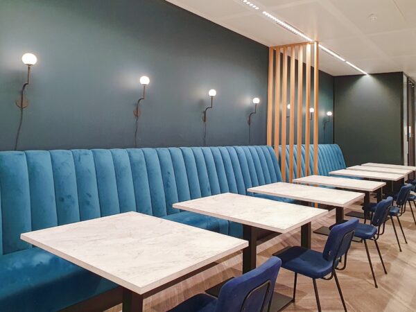 Moderne zitruimte met blauwe fluwelen banken, marmeren tafels en wandlampen aan een donkergroene muur in Stadsplateau 7.