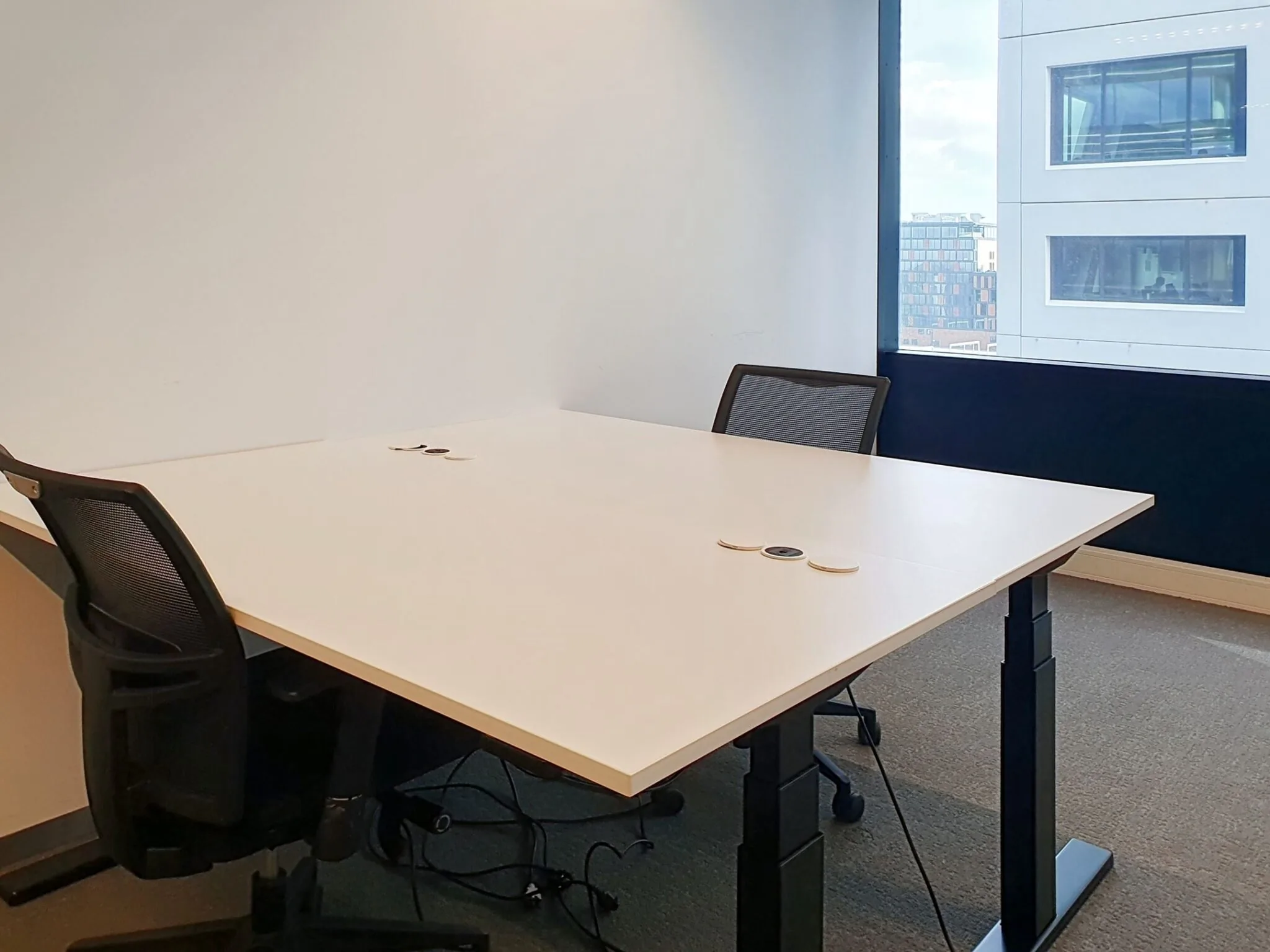 Twee bureaustoelen staan aan een groot wit bureau in een moderne kantoorruimte met uitzicht op omliggende gebouwen.