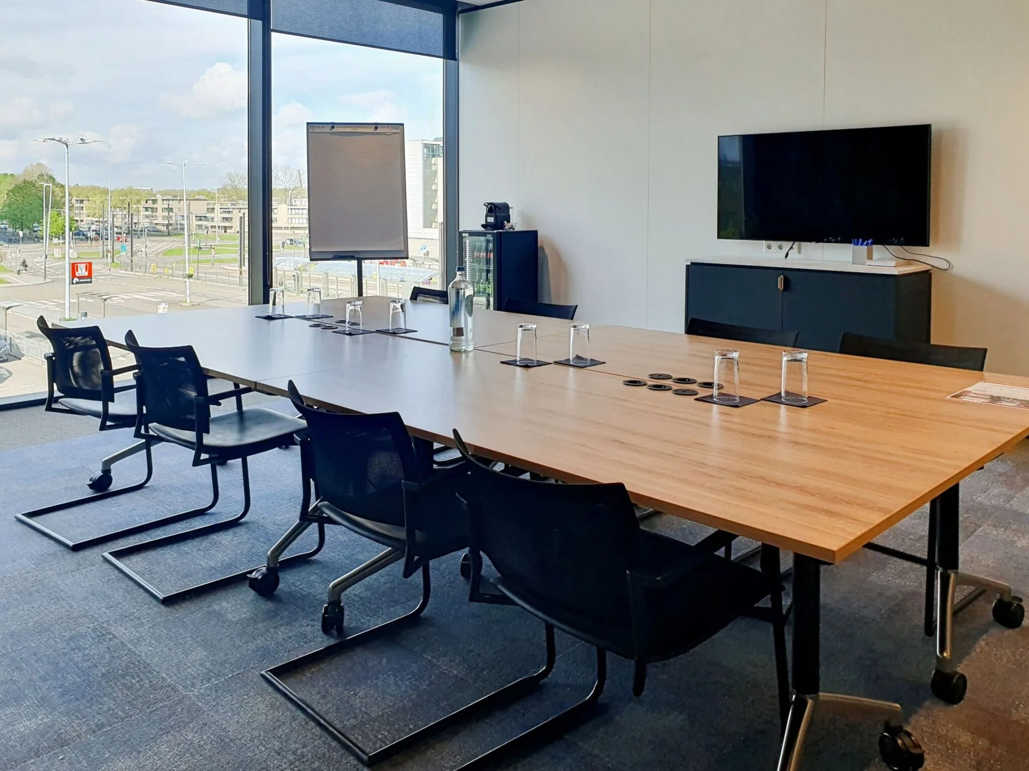 Vergaderruimte op Stadsplateau 7 met groot raam, vergadertafel, stoelen, tv en flip-over.