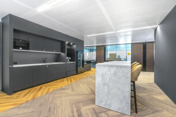 Moderne kantoorpantry met donkere kasten, marmeren bar en houten visgraatvloer in Stadsplateau 7.