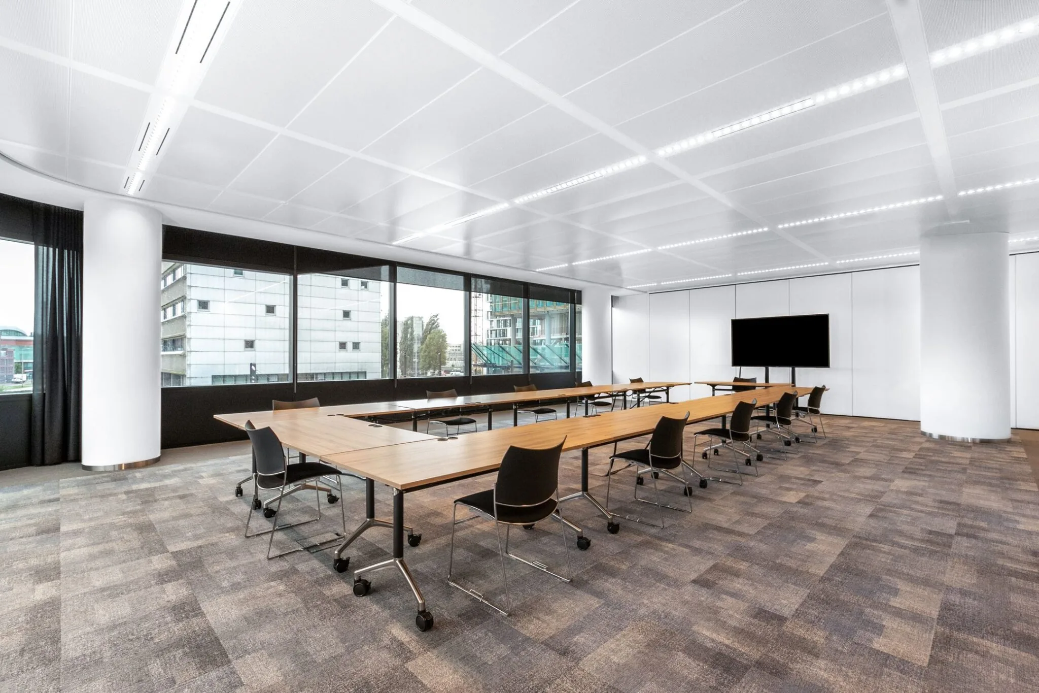 Moderne vergaderruimte met grote ramen, lange houten tafels, zwarte stoelen en een flatscreen, gelegen in Stadsplateau 7.