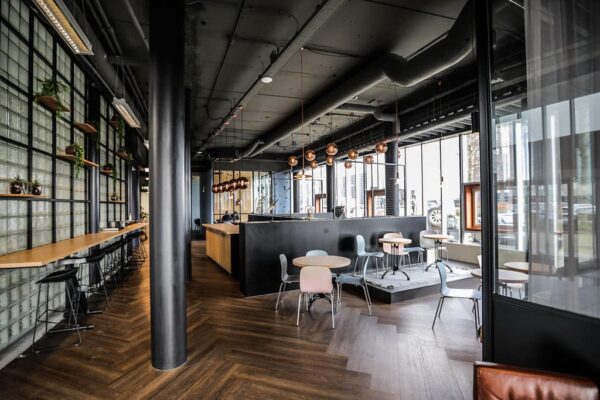 Moderne horecaruimte aan de Statenlaan 1-27 met industrieel interieur, houten vloer, glazen wanden en een centrale bar.