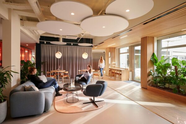 Moderne en lichte loungeruimte in Statenlaan 1-27 met zitmeubels, planten en houten accenten.