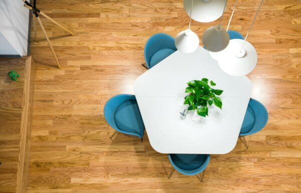 Wit vierkant tafelblad met plant en vier blauwe stoelen op houten vloer, gezien van bovenaf.