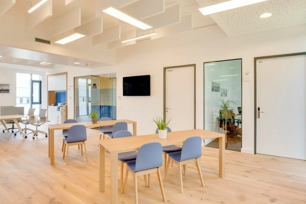 Moderne kantoorruimte aan Stationsplein 18 met houten vloeren, lichte tafels, blauwe stoelen en glazen vergaderruimte.