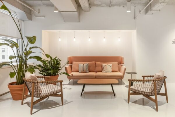 Moderne wachtruimte met een roze bank, twee rotan stoelen, hanglampen en grote kamerplanten in Stationsplein 18.