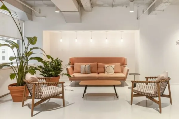 Moderne wachtruimte met een roze bank, twee rotan stoelen, hanglampen en grote kamerplanten in Stationsplein 18.