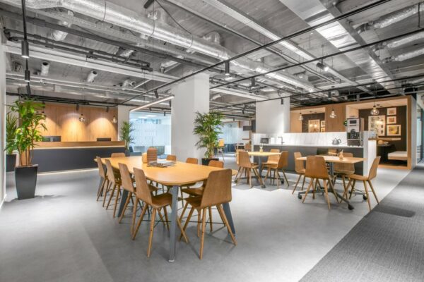 Moderne gemeenschappelijke werkruimte met houten meubels, planten en een open keuken in het kantoorgebouw op Stationsplein 18.