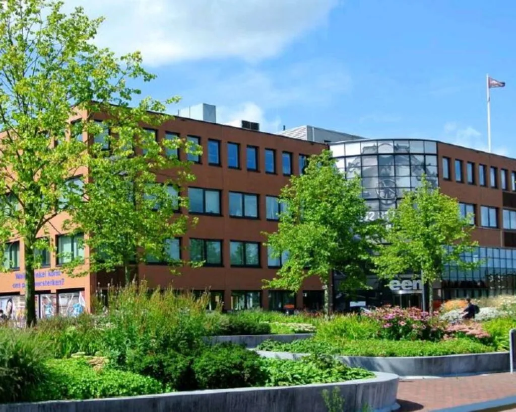 Kantoorgebouw aan het Stationsplein met een tuin vol groen en bloemen op de voorgrond.