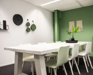 Moderne vergaderruimte met een grote witte houten tafel, omringd door witte stoelen en groene accenten in het interieur.