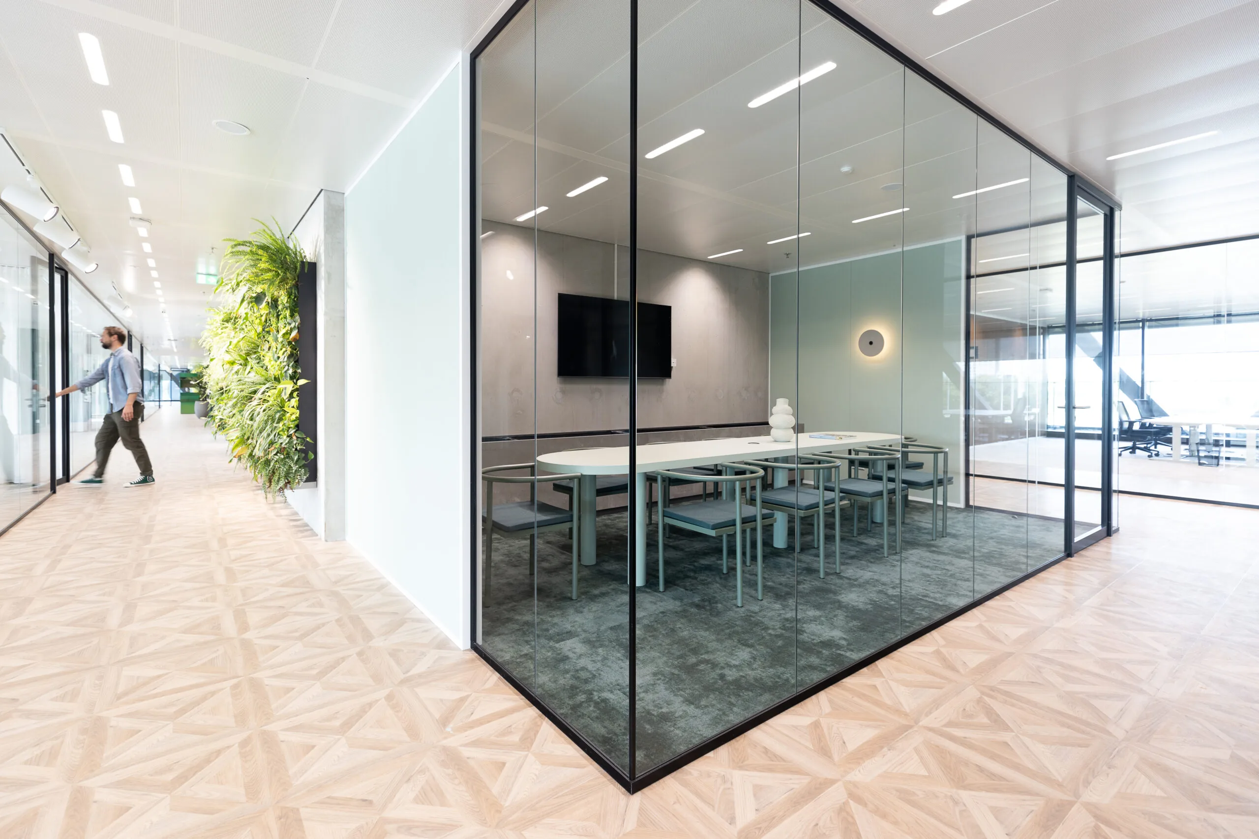 Vergaderruimte The Joan-18 met glazen wanden, moderne inrichting en een groene plantenwand in de gang.