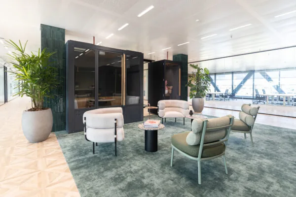 Moderne en stijlvolle loungehoek in kantoorruimte The Joan-2 met designstoelen, planten en glazen vergaderruimtes.