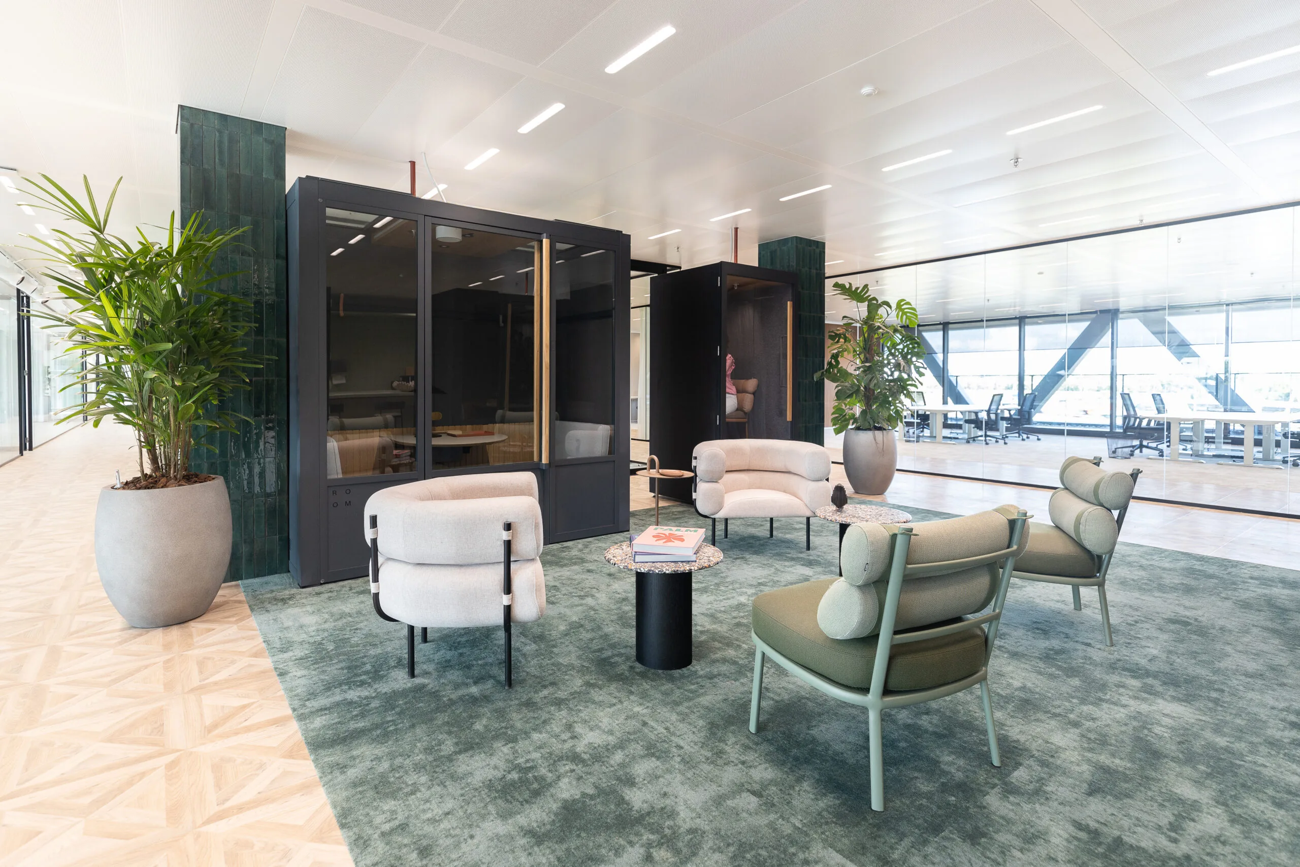 Moderne en stijlvolle loungehoek in kantoorruimte The Joan-2 met designstoelen, planten en glazen vergaderruimtes.