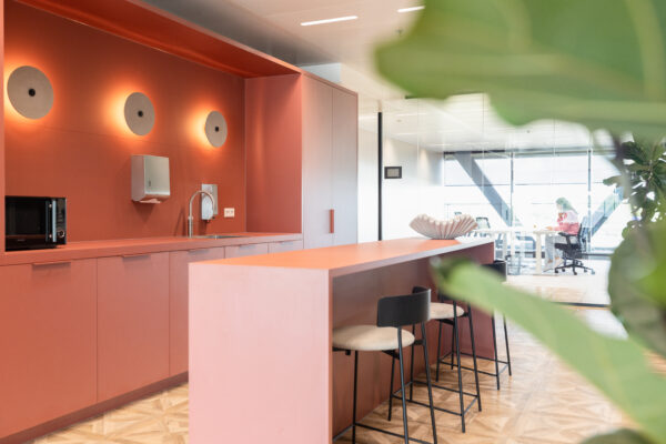 Moderne keukenruimte in The Joan-21 met roodkleurig interieur, een hoge tafel en zicht op een glazen kantoorruimte.