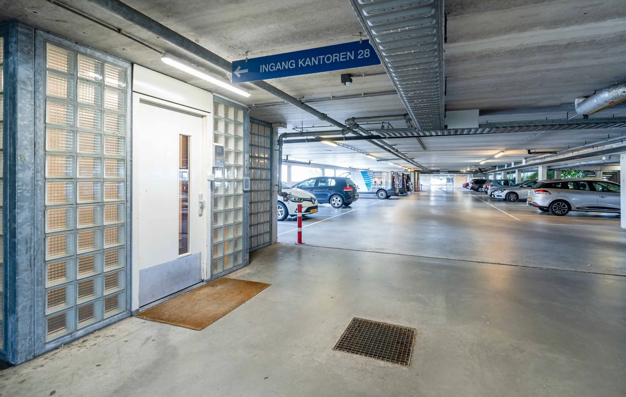 Overdekte parkeergarage bij Tielweg 30 met glazen entree naar kantoren en geparkeerde auto's.