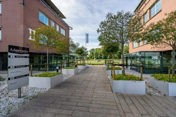 Ingang van het Mercator bedrijfsgebouw aan de Tielweg met moderne beplanting en zicht op gebouwen 26 en 28.