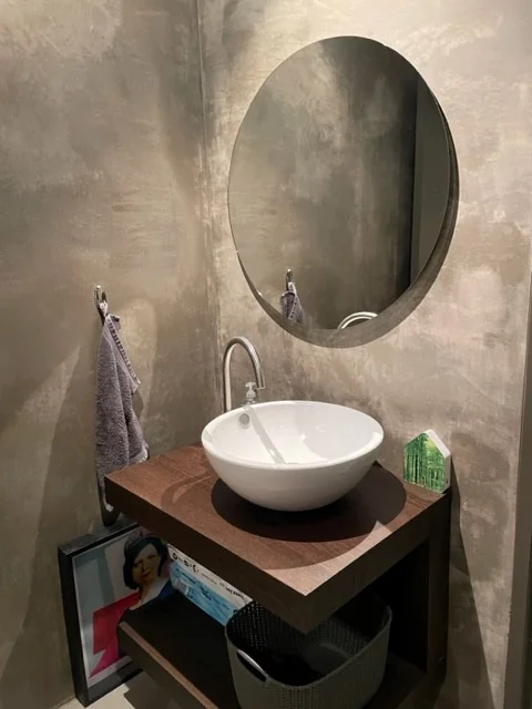 Moderne toiletruimte met ronde spiegel, waskom op houten blad en minimalistische decoratie.
