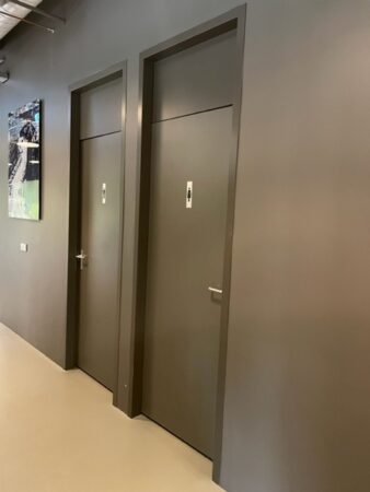 Twee grijze toiletdeuren met mannelijke en vrouwelijke pictogrammen in een moderne, donkere gang.