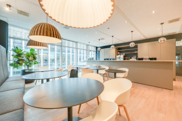 Een moderne kantoorruimte met een open zithoek, ronde tafels, designstoelen, en grote ramen bij Tribes Amsterdam SOM.