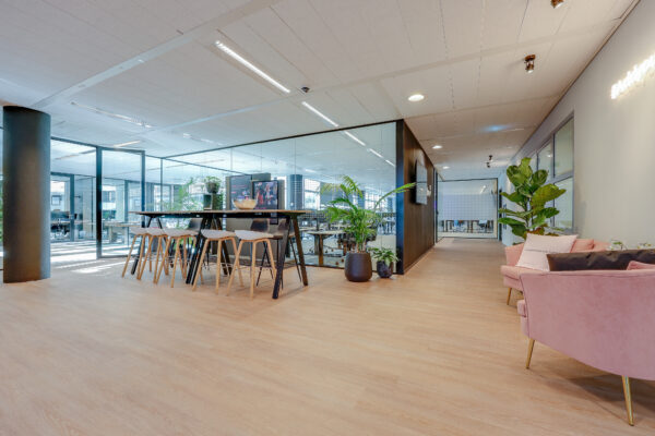 Een moderne kantoorlounge bij Tribes Amsterdam SOM met glazen wanden, planten en stijlvolle houten meubels.