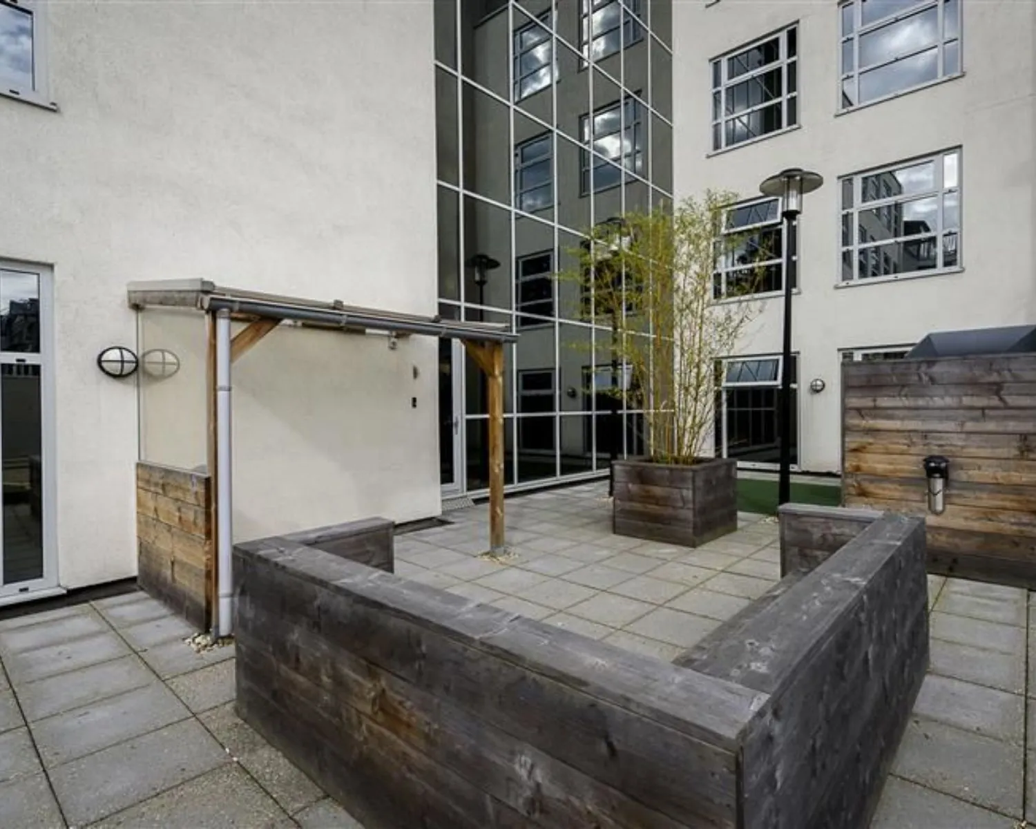 Moderne binnentuin met houten plantenbakken en zitgedeelte, omringd door hoge kantoorgebouwen met spiegelende ramen.