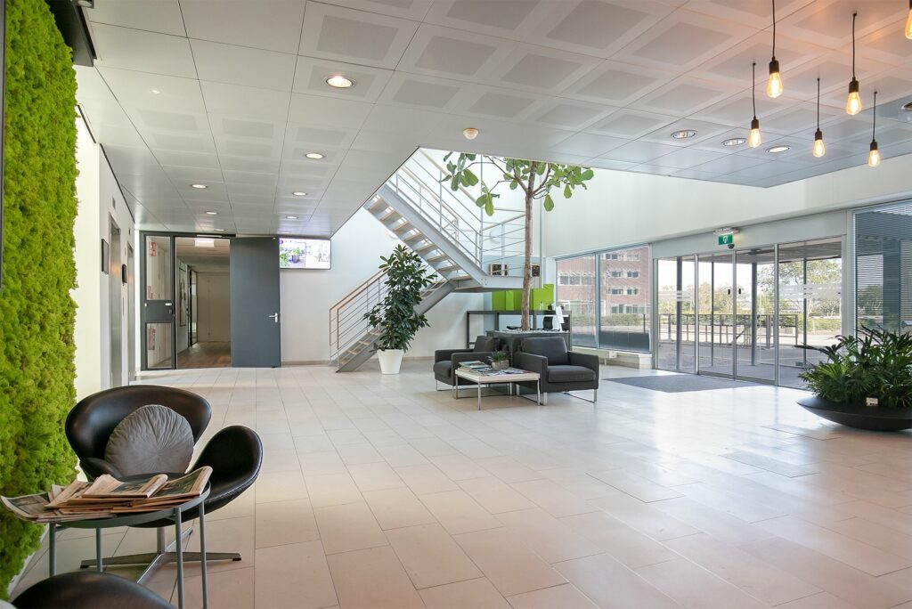 Moderne en lichte ontvangsthal van het kantoorgebouw aan de Tupolevlaan 41 met zithoek, planten en trap naar boven.