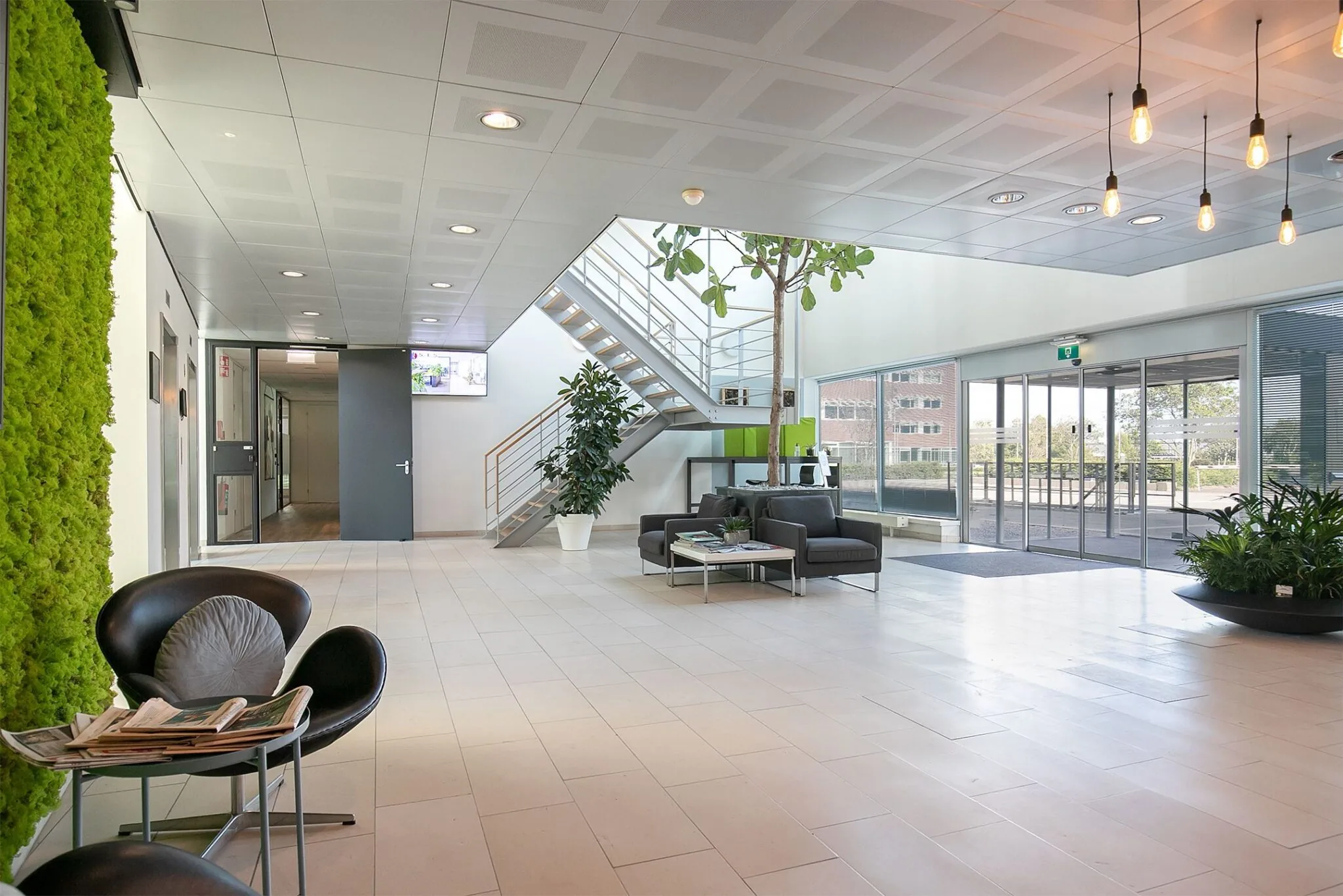 Moderne en lichte ontvangsthal van het kantoorgebouw aan de Tupolevlaan 41 met zithoek, planten en trap naar boven.