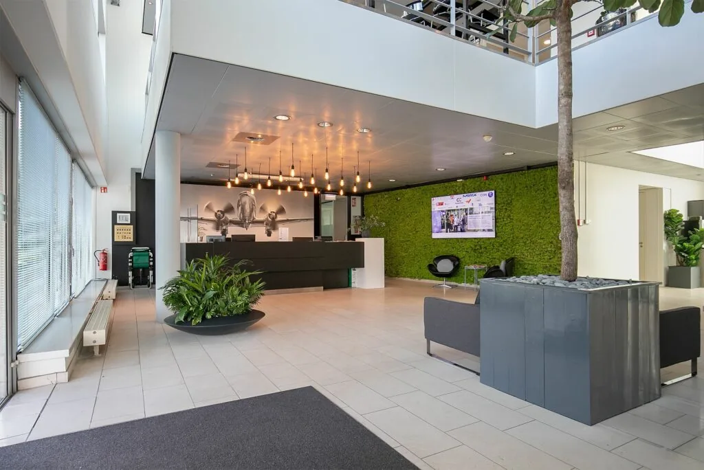 Moderne ontvangsthal van Tupolevlaan 41 met een balie, groene moswand, grote plant en vliegtuigfoto aan de muur.