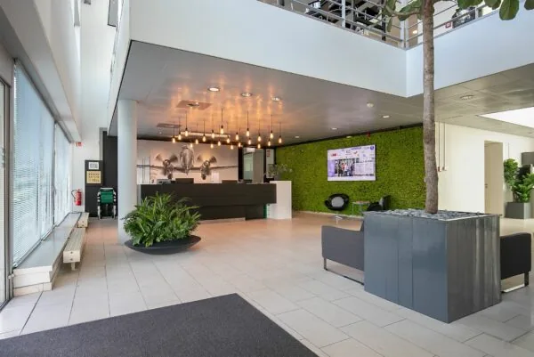 Moderne ontvangsthal van Tupolevlaan 41 met een balie, groene moswand, grote plant en vliegtuigfoto aan de muur.