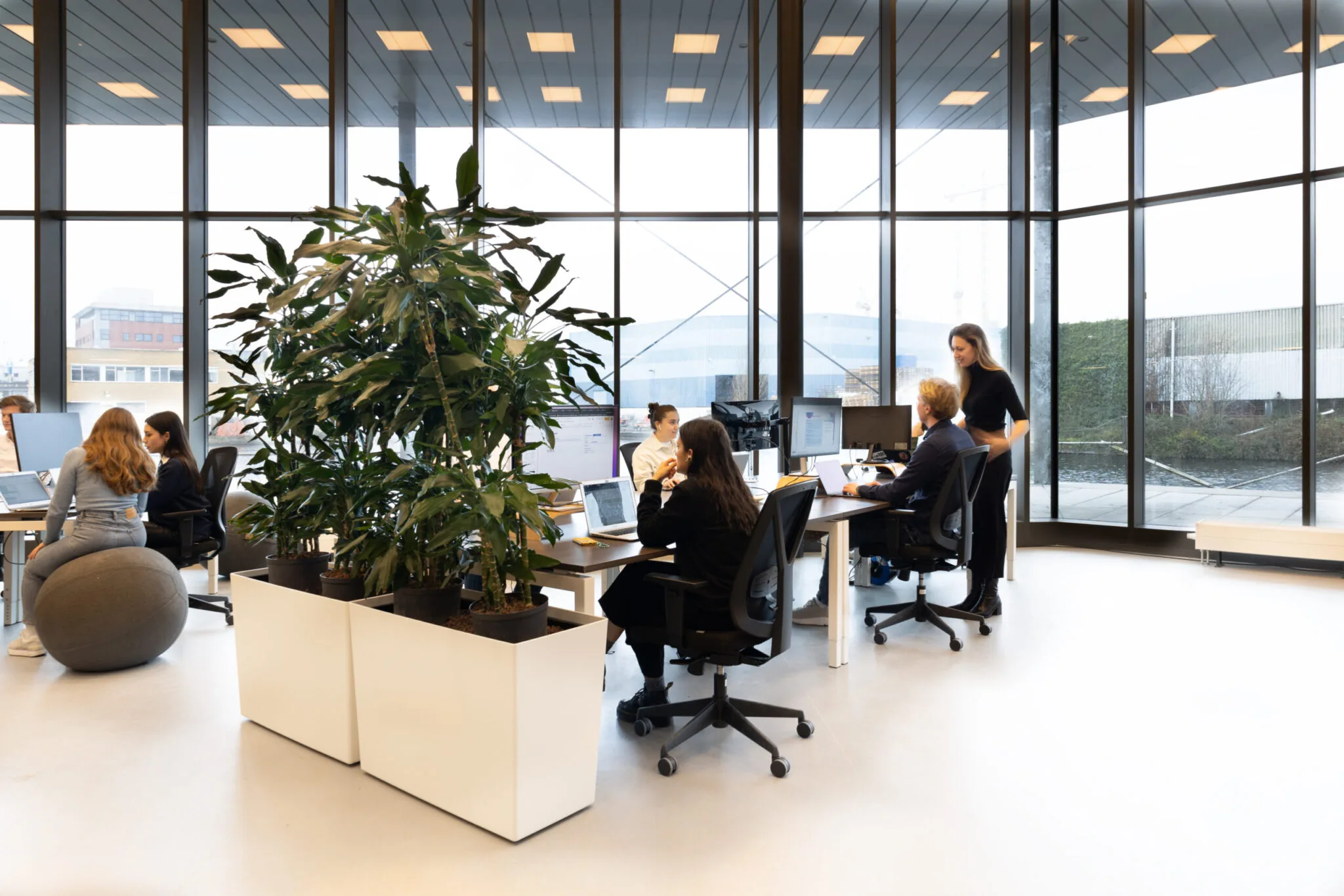 Moderne kantoorruimte in Unknown Spaces Titaan 07 met werkende mensen aan bureaus en grote ramen op de achtergrond.