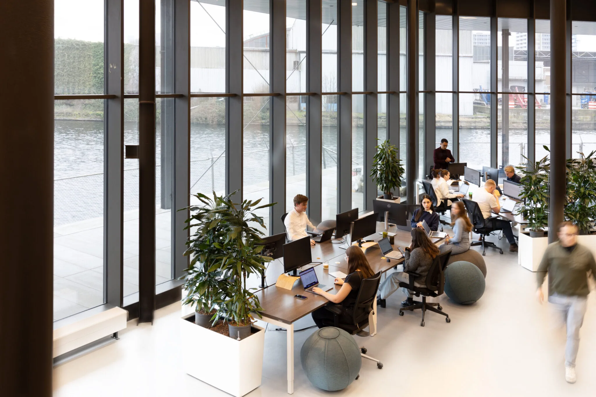 Open kantoorruimte in Unknown Spaces Titaan 08 met werkende mensen aan bureaus naast grote ramen met uitzicht op het water.
