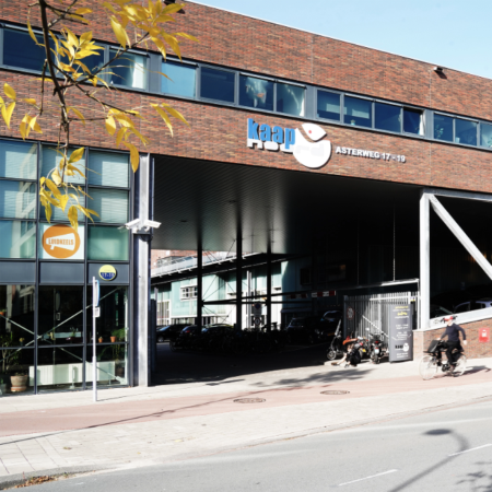 Een stadsgebouw met het bord "kaap asterweg 17-19" en een fietser op de voorgrond.