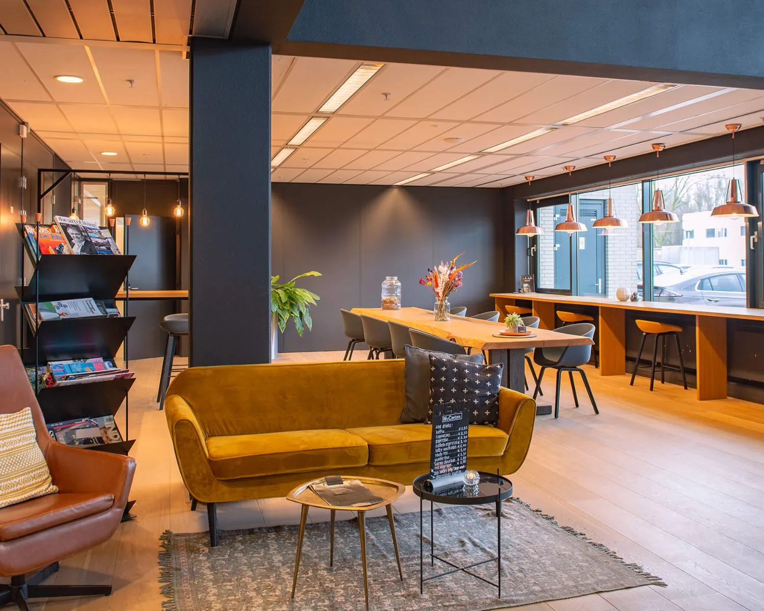 Modern ingerichte lounge- en werkruimte in een kantoor in Utrecht met zithoek, leestafel en hoge werkplekken bij het raam.
