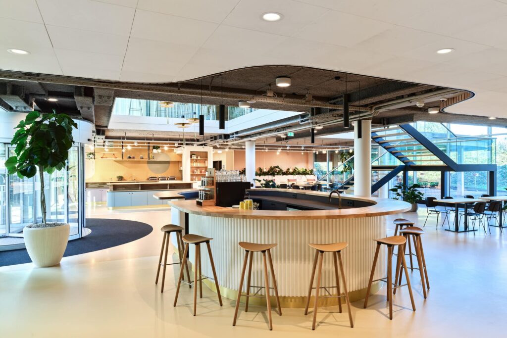 Moderne kantoorruimte aan de Van Deventerlaan 30-40 met een ronde koffiebar, zitplekken en een open trap naar de bovenverdieping.