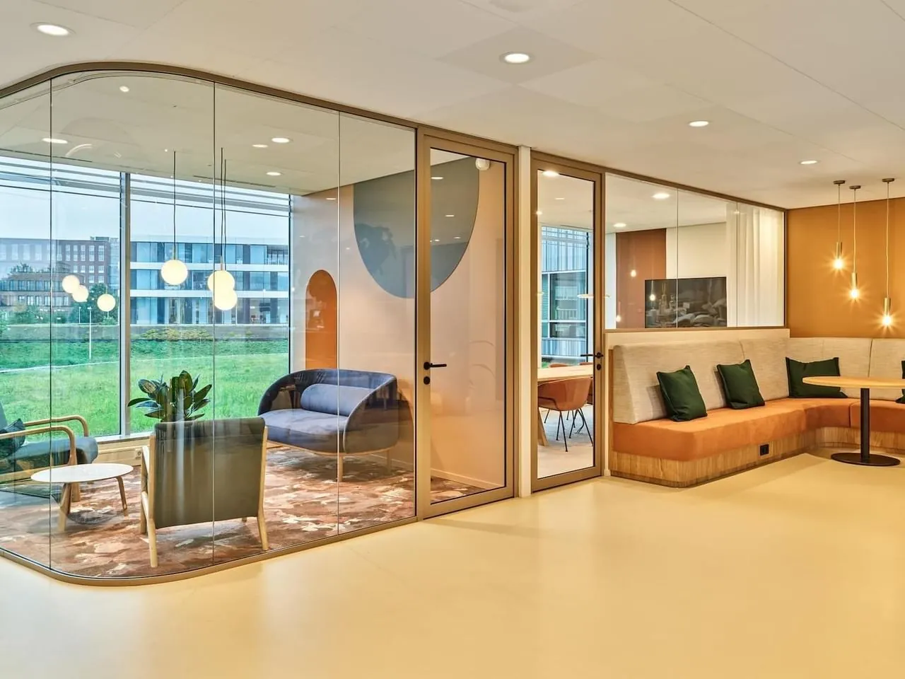 Modern ingerichte kantoorlounge aan de Van Deventerlaan 30-40 met glazen vergaderruimte en zithoek met oranje banken en hanglampen.