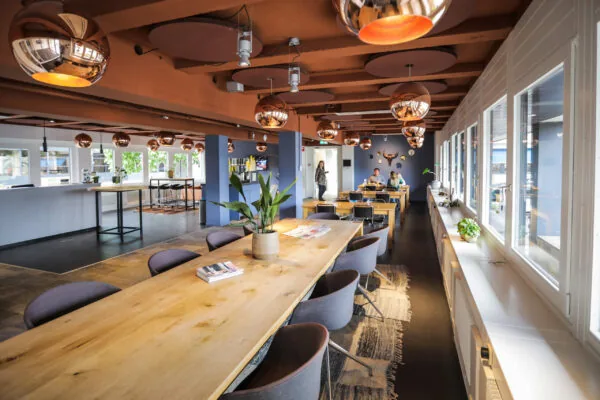 Moderne, sfeervolle kantine in Van Deventerlaan 30-40 met houten tafels, designverlichting en grote ramen.