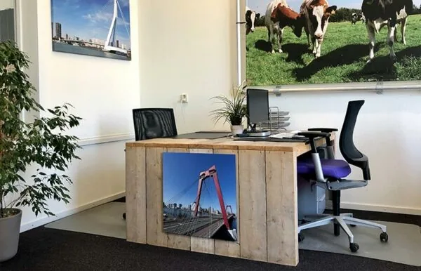 Modern ingericht kantoortje met houten bureau, kantoormeubilair en foto's van Rotterdam en koeien aan de muur.