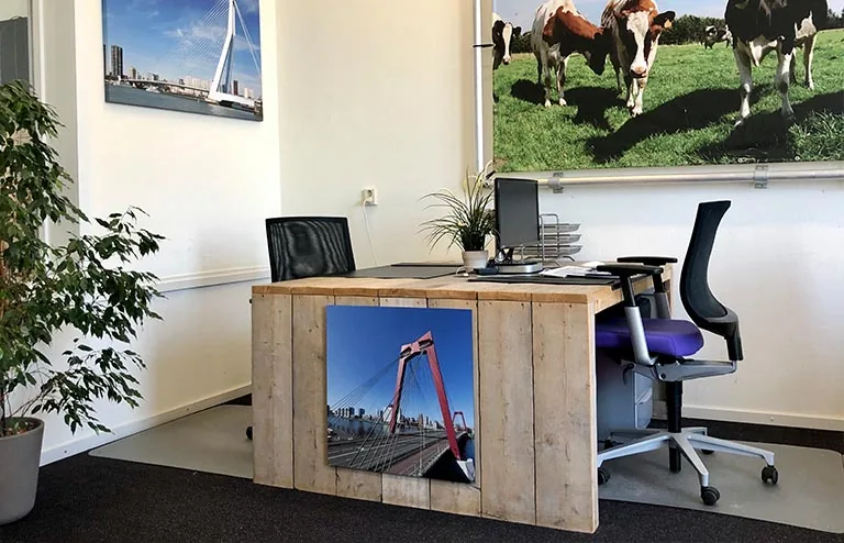 Modern ingericht kantoortje met houten bureau, kantoormeubilair en foto's van Rotterdam en koeien aan de muur.