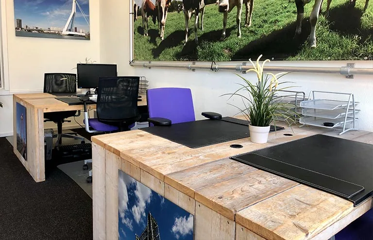 Moderne kantoorruimte aan de Van der Takstraat 8 met houten bureaus, bureaustoelen en grote wandfoto’s van Rotterdam en koeien.