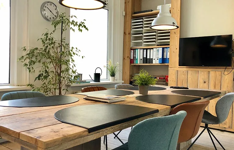 Vergaderruimte aan de Van der Takstraat 8 met houten tafel, gekleurde stoelen, ordners en een flatscreen-tv.