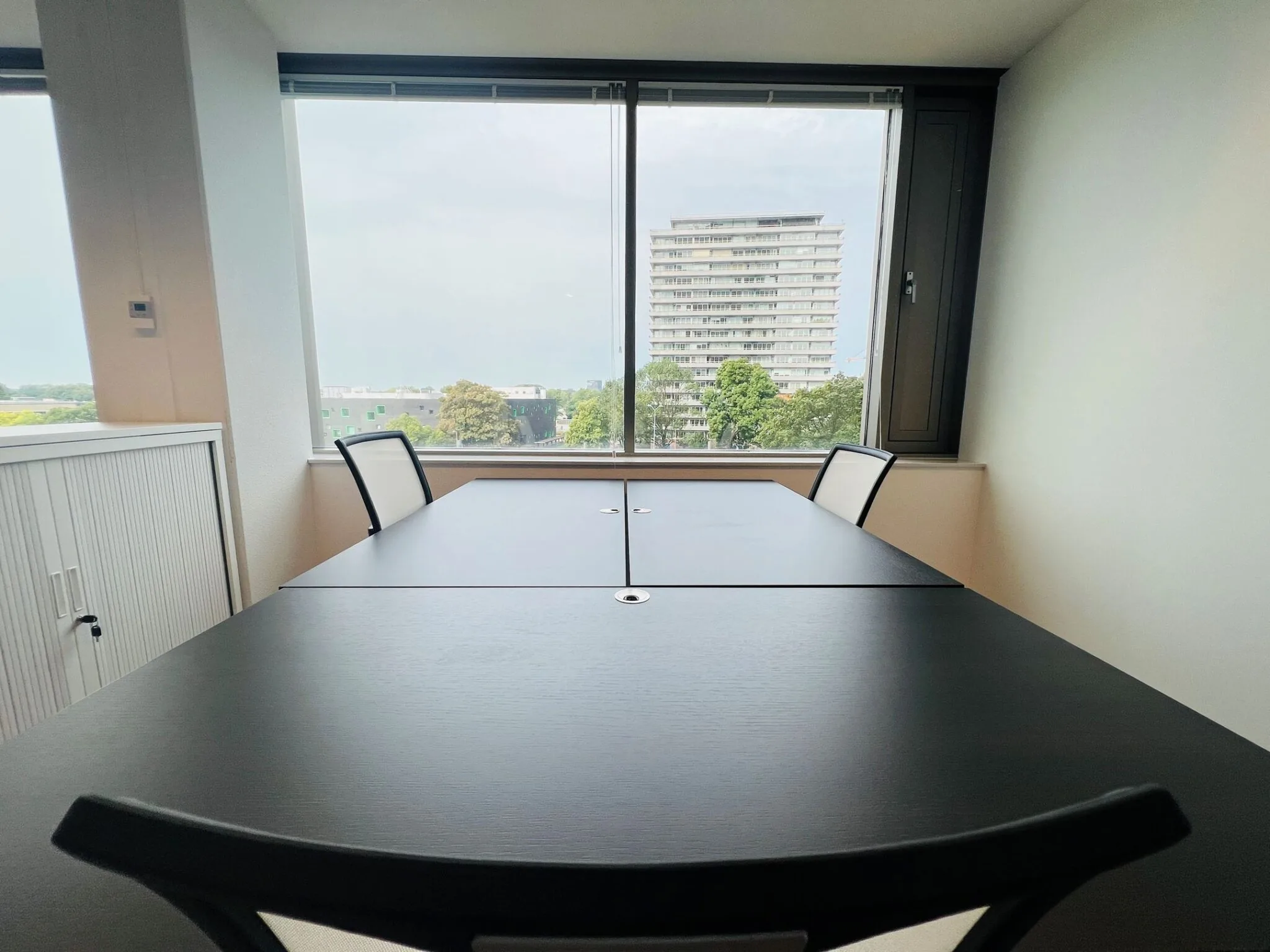 Vergaderruimte met twee stoelen en uitzicht op een woongebouw vanaf Vliegend Hertlaan 21.