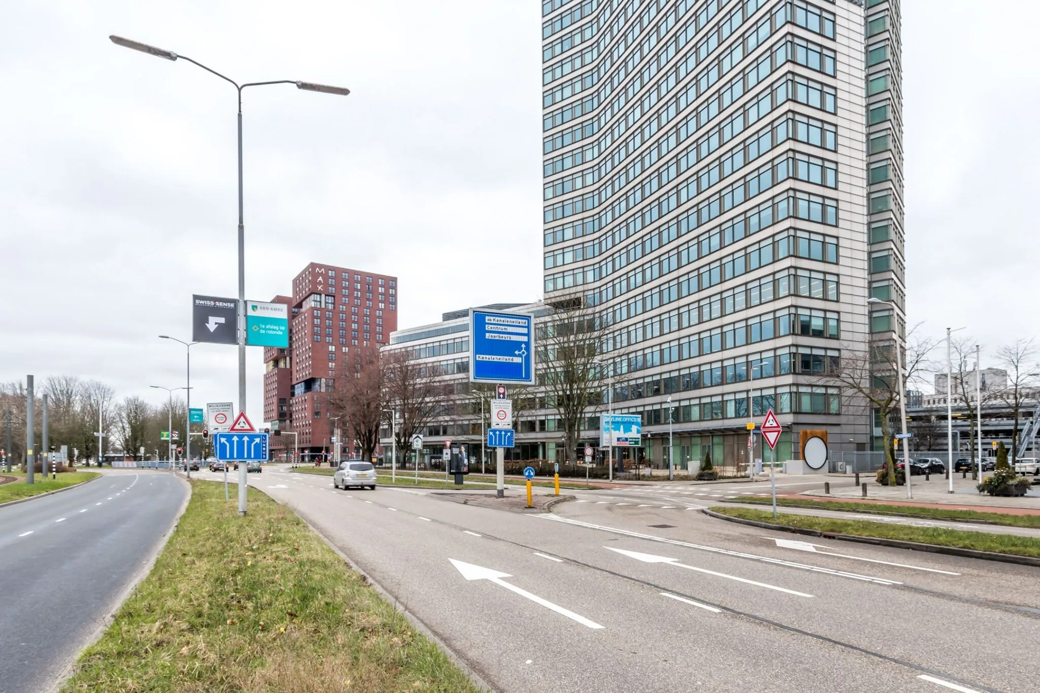 Drukke straat bij Vliegend Hertlaan 21 met hoog kantoorgebouw en verkeersborden in beeld.